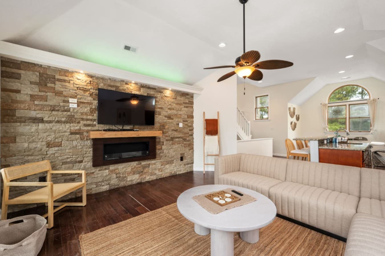 Living room w/ stone accent wall, mounted TV, electric fireplace & a long sectional below vaulted ceilings.