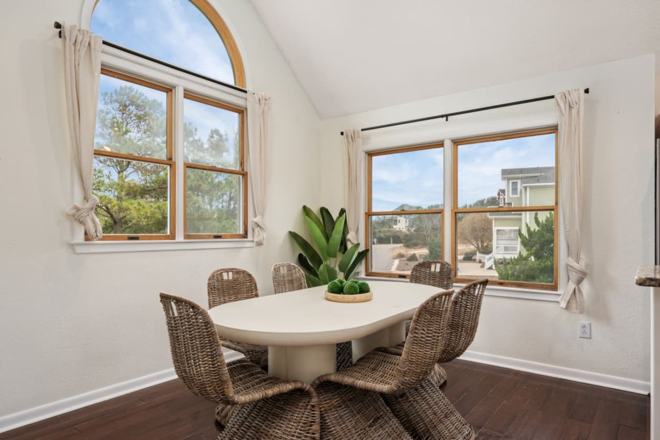 Dining nook w/ oval table, woven chairs & an arched window under a vaulted ceiling.