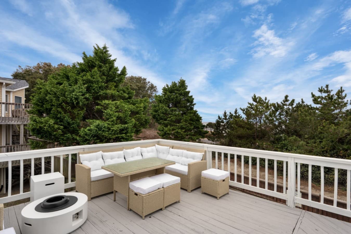 Top-level deck w/ wicker sectional, ottomans & open sky above the treetops.