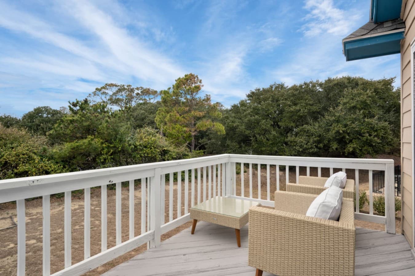 Mid-level deck w/ wicker armchairs & an ottoman looking out over the maritime treeline.