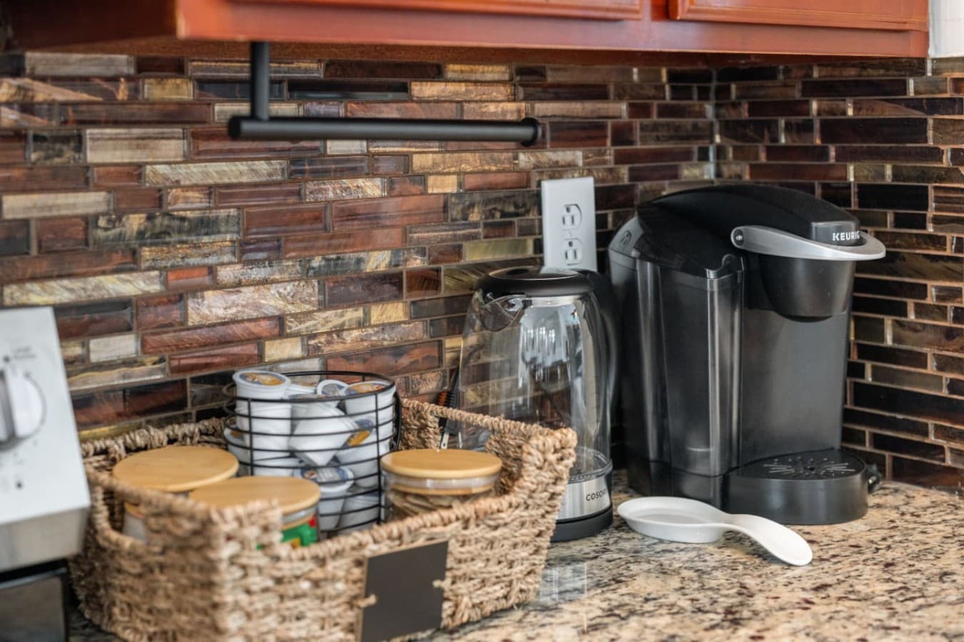 Coffee corner against the brick backsplash w/ brewer, mugs & pods kept in a basket.