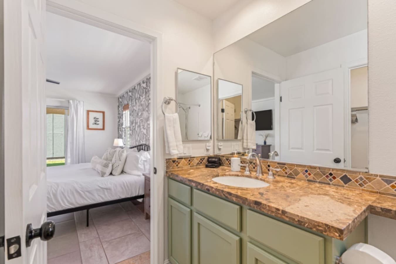 Primary bedroom view w/ plush bedding, accent wall & easy access to the bathroom.