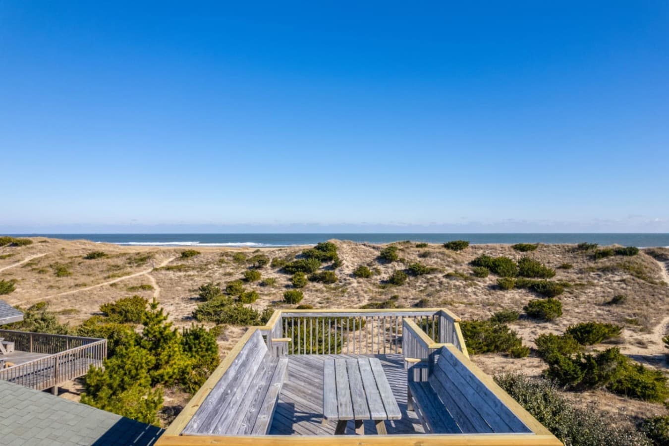 Panoramic deck view overlooking the coastline, dunes & sparkling blue water beyond.