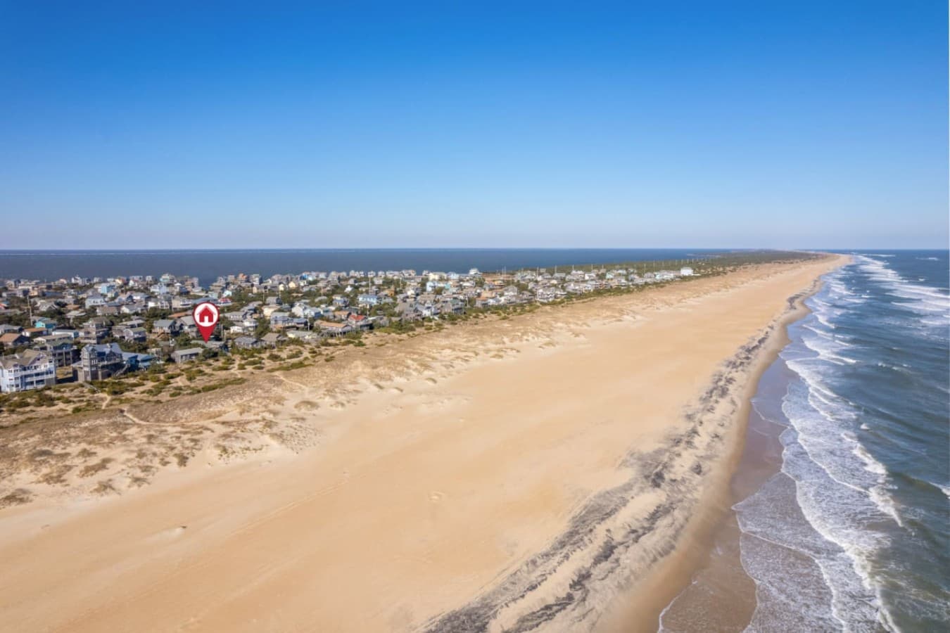 Sweeping shoreline view w/ waves rolling in & beach homes lining the coast.