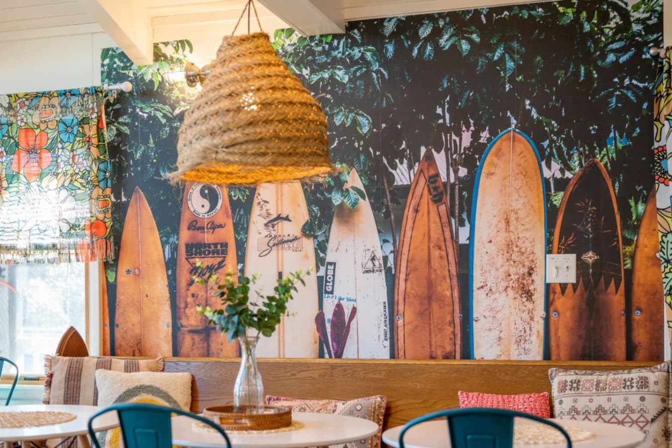 Surfboard accent wall w/ woven lighting & greenery for a bold, beachy statement.