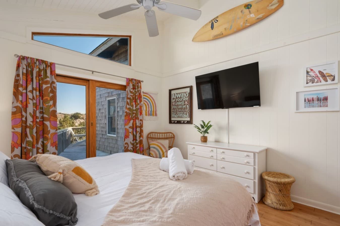 Bright bedroom w/ patterned curtains, wall-mounted TV & natural light throughout.