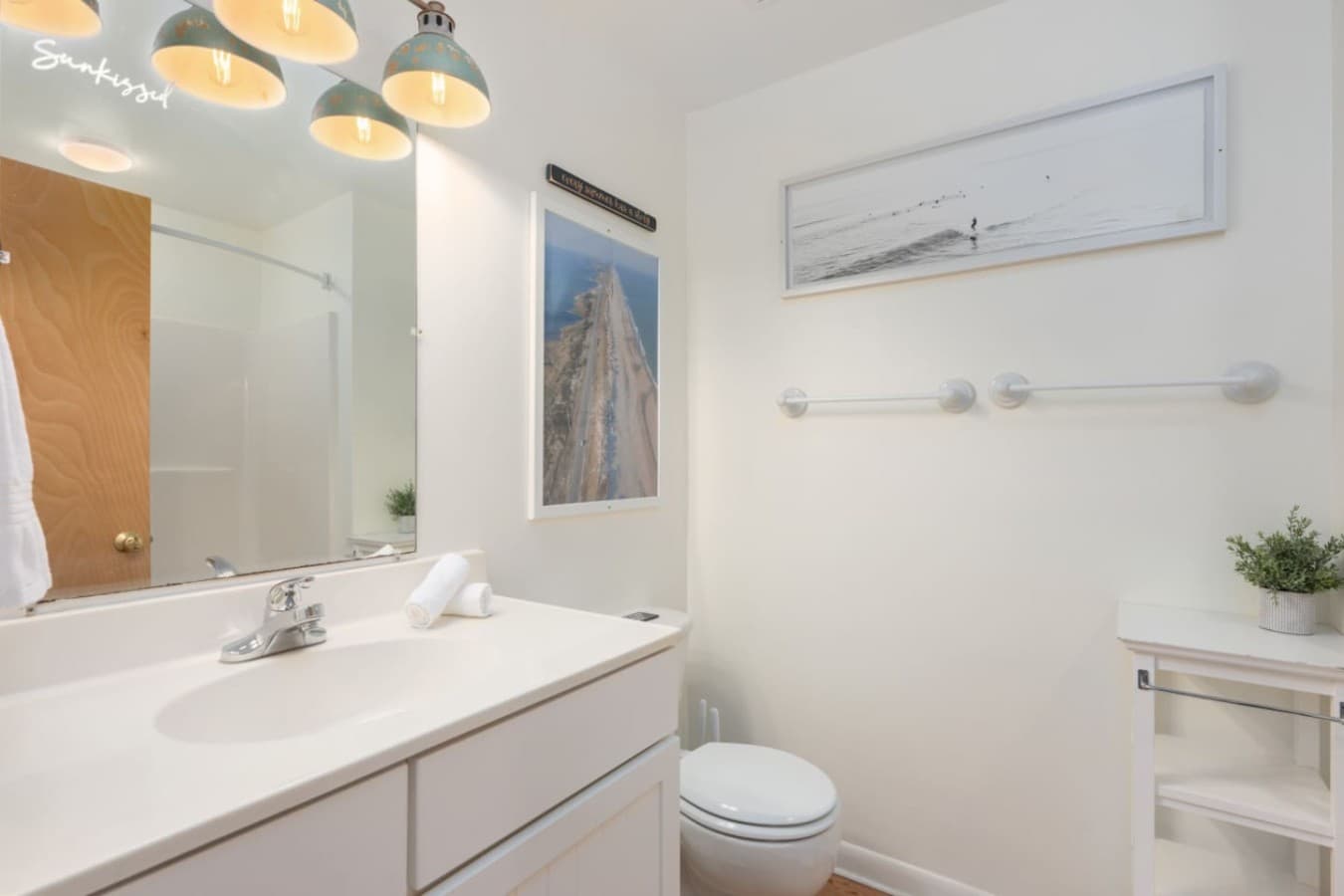 Clean bathroom vanity w/ wide mirror, bright lighting & crisp white finishes.
