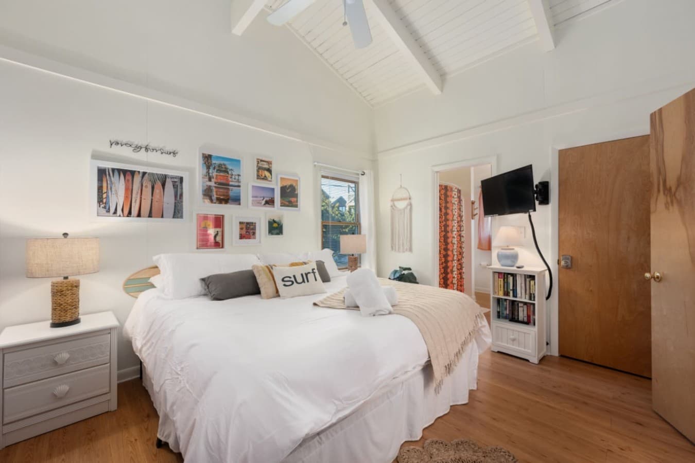 Bedroom under a vaulted plank ceiling w/ crisp white bedding, gallery wall & a TV.
