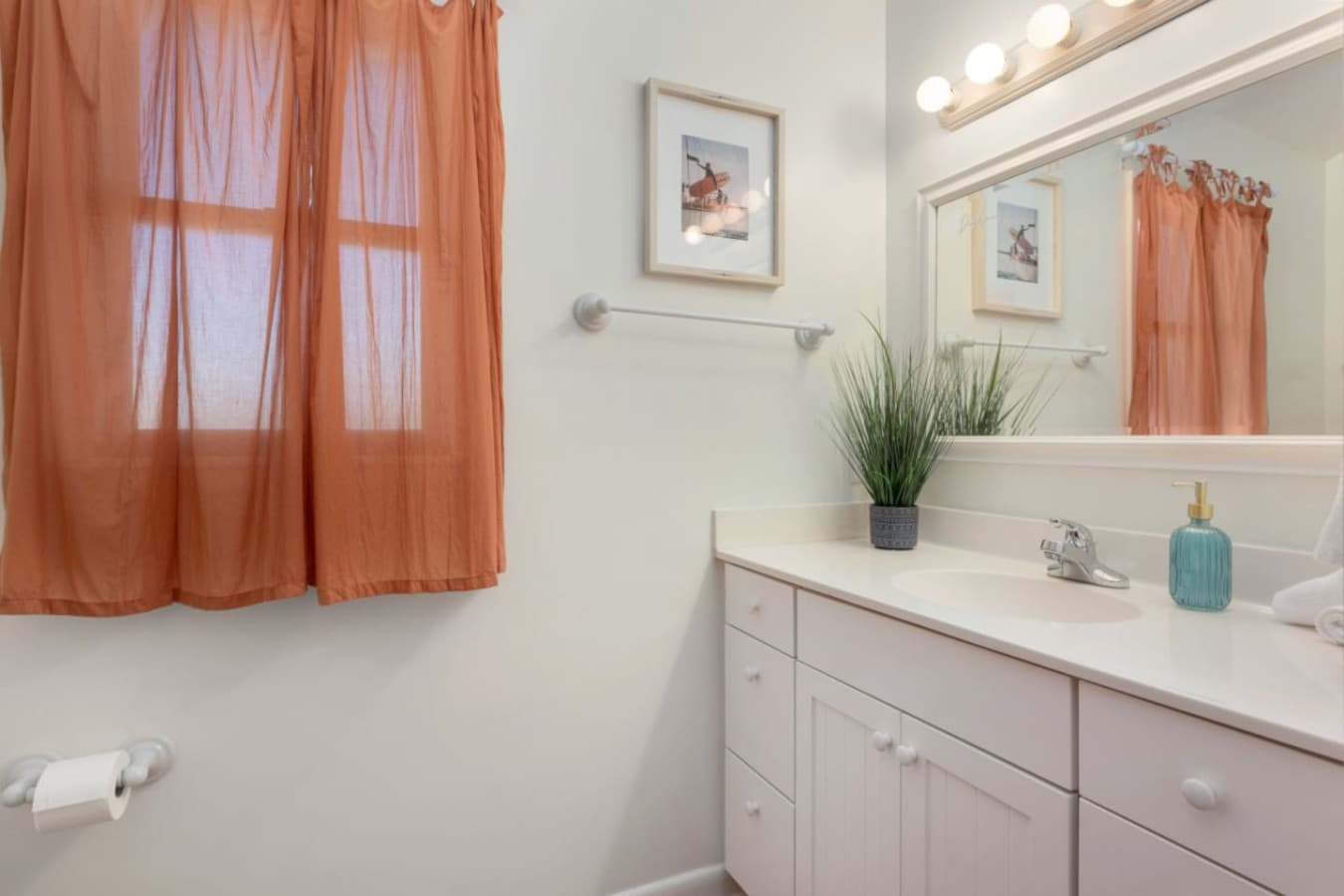 Bathroom vanity w/ framed mirror, vanity lighting & a curtained window for soft daylight.