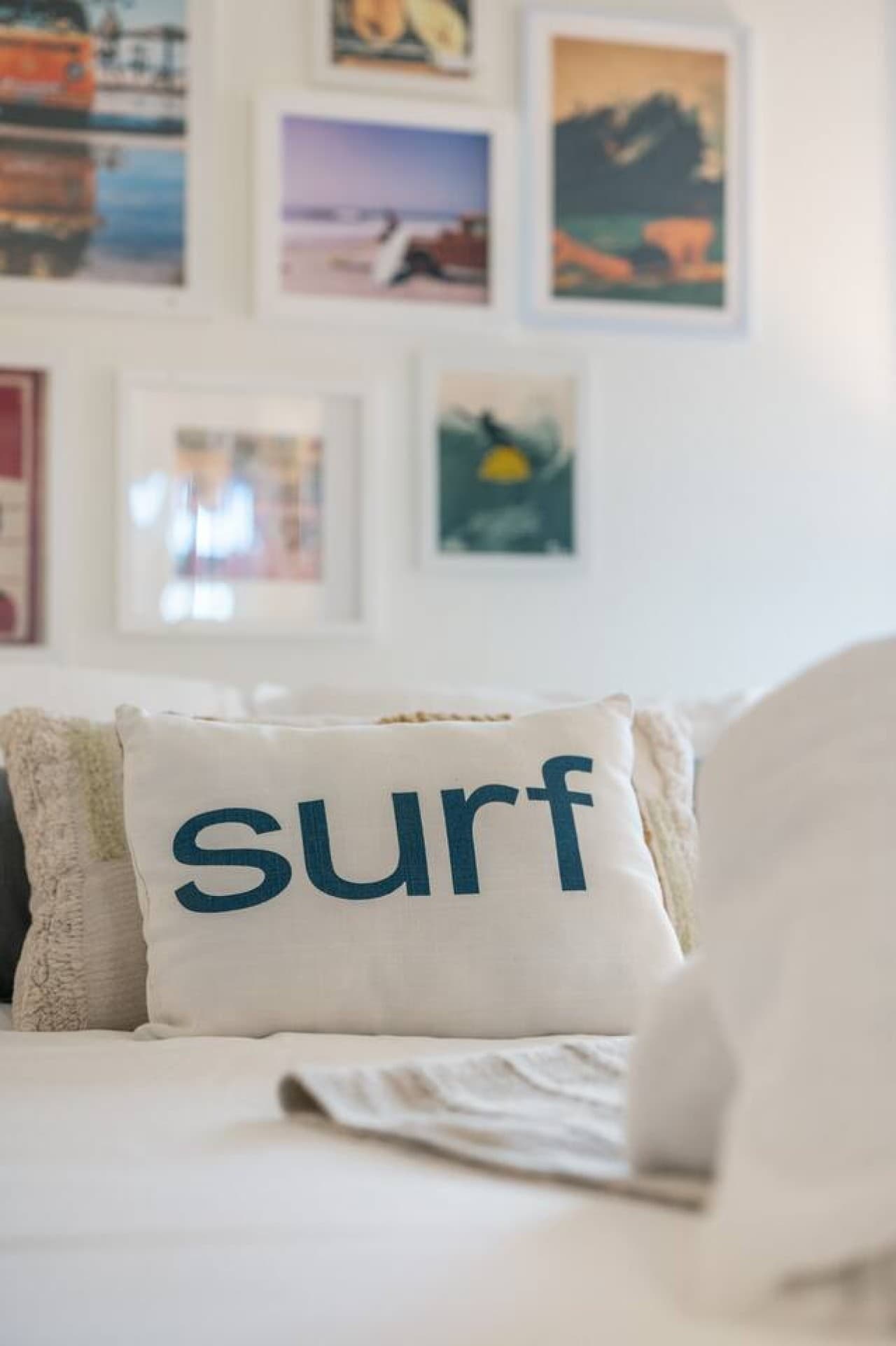 Detail of the bed made up in crisp white linens w/ a surf pillow & beach photo wall.