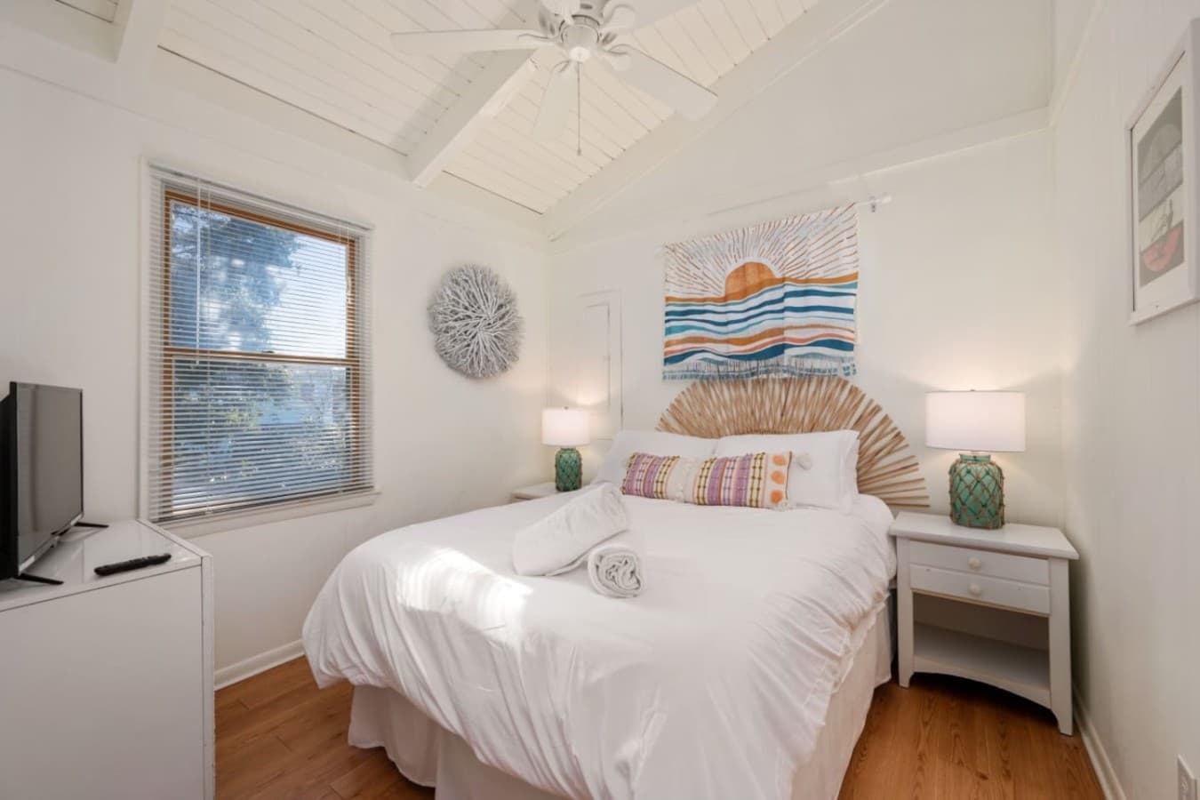 Bedroom w/ woven wall art, matching nightstand lamps & a TV for slow mornings.