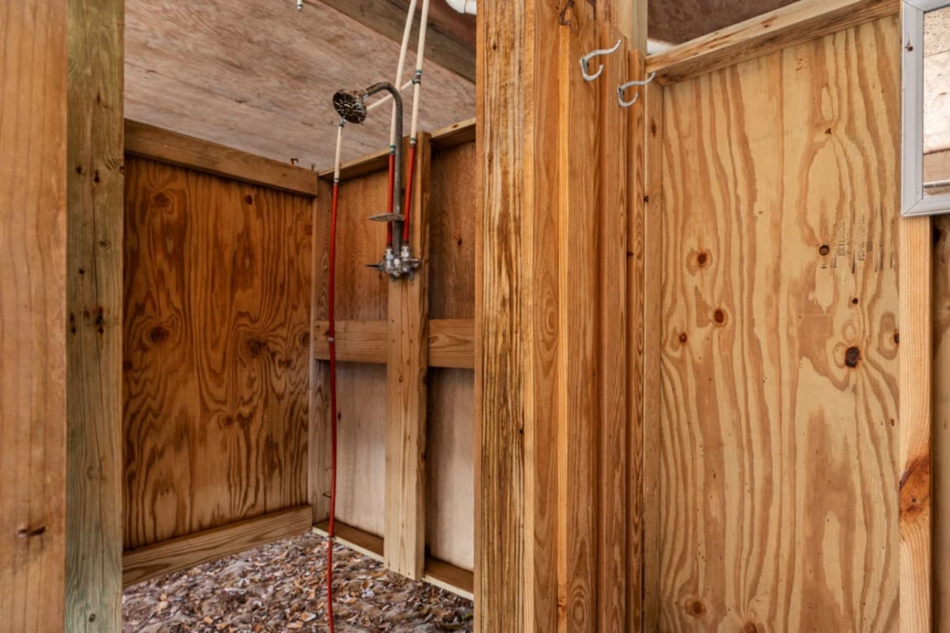 Enclosed outdoor shower w/ wood walls & a pebble floor for rinsing off after the beach.