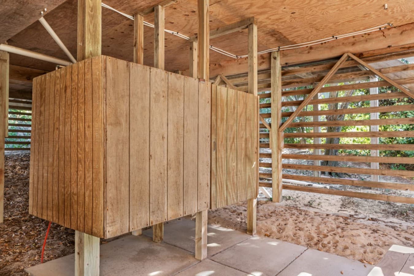 Wood-walled outdoor shower & changing stalls set on the sand beneath the house.