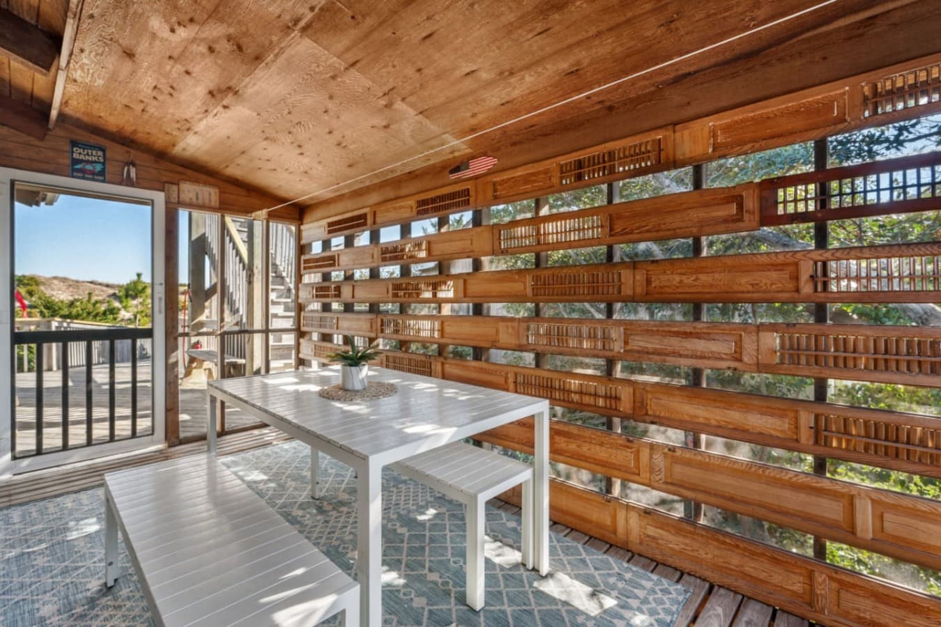 Slatted breezeway dining area w/ a white table, benches & dune views through the walls.