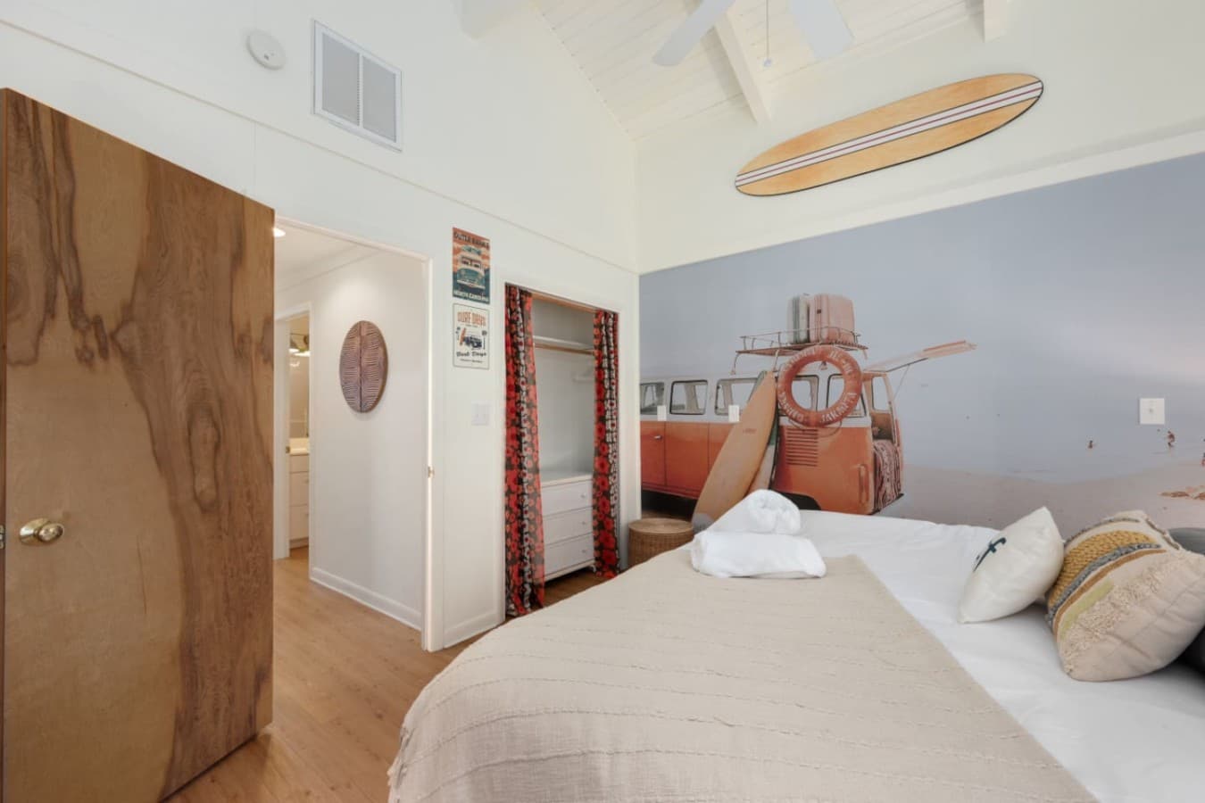 Bedroom w/ a mounted surfboard, beach mural wall & curtained closet under a vaulted ceiling.
