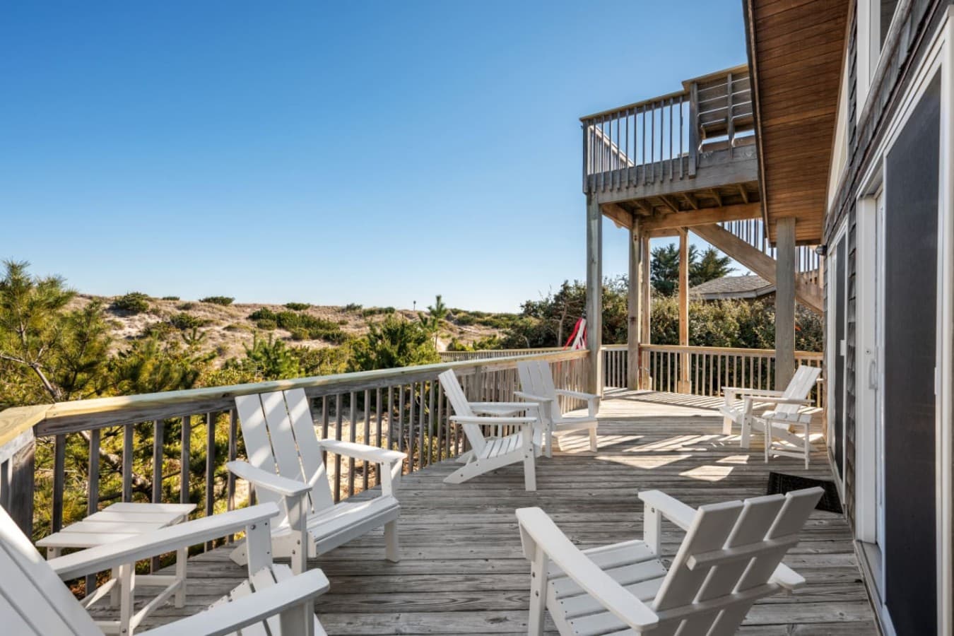Sun deck w/ white Adirondack chairs & stairs to the upper level, dunes just beyond.