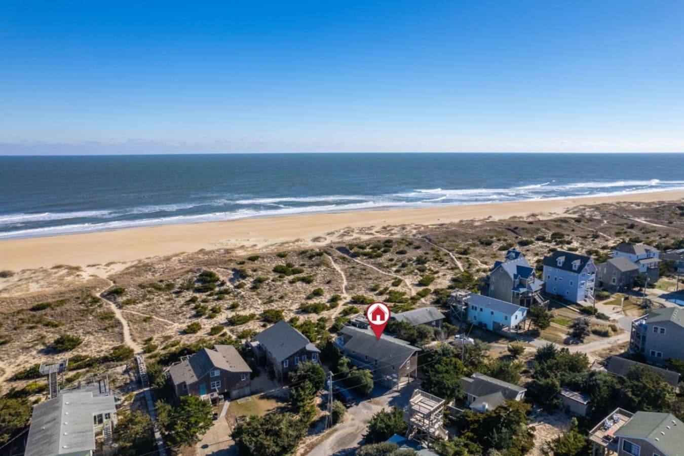 Aerial showing the house tucked just behind the dune w/ the beach and ocean beyond.