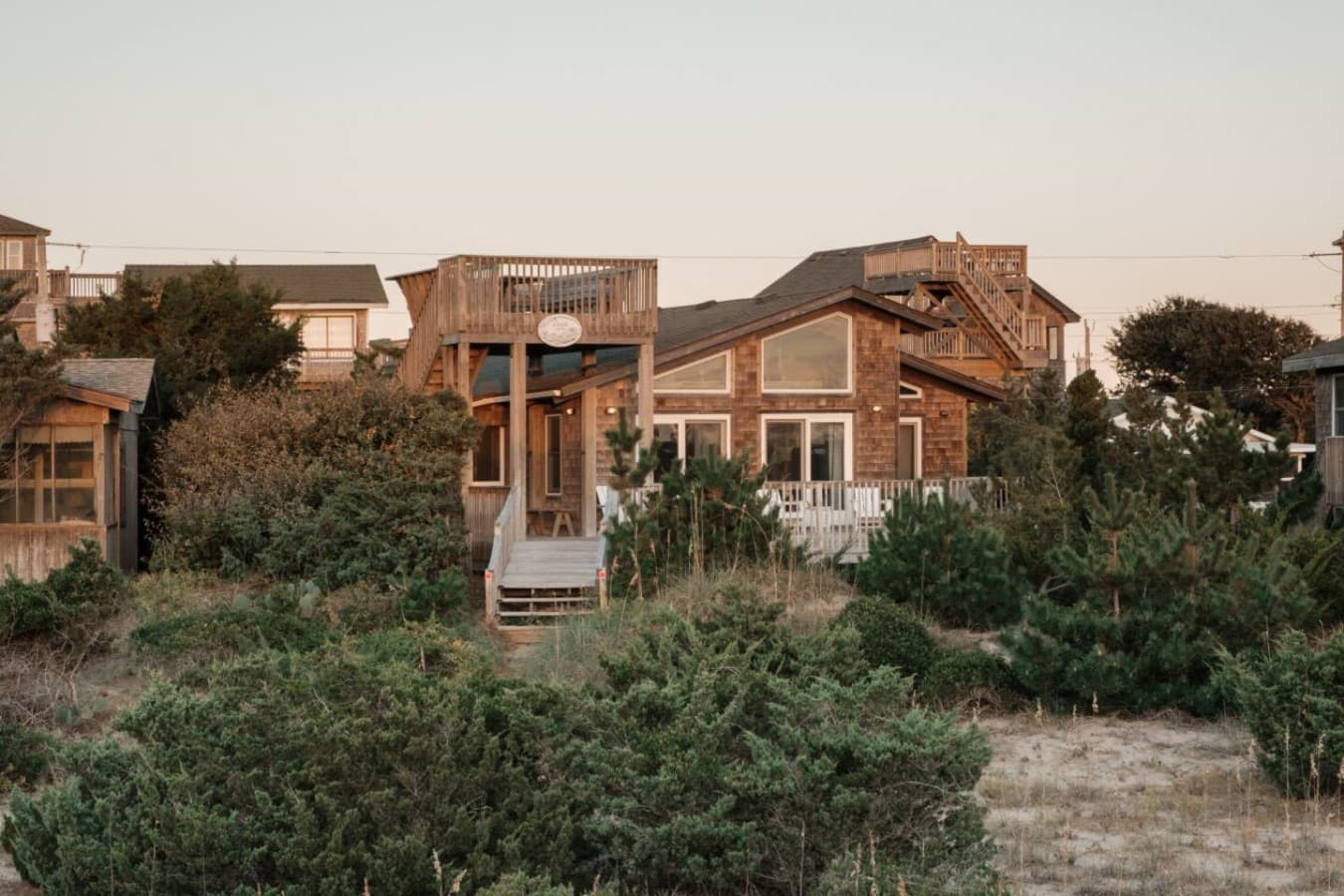 The cedar-shake cottage seen from the dune at golden hour, framed by sea grass.