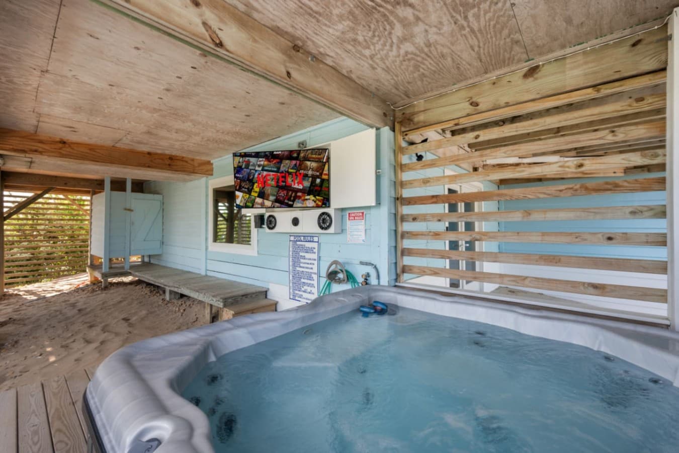 Covered hot tub deck w/ a wall-mounted TV, slatted privacy screen & wood plank ceiling.