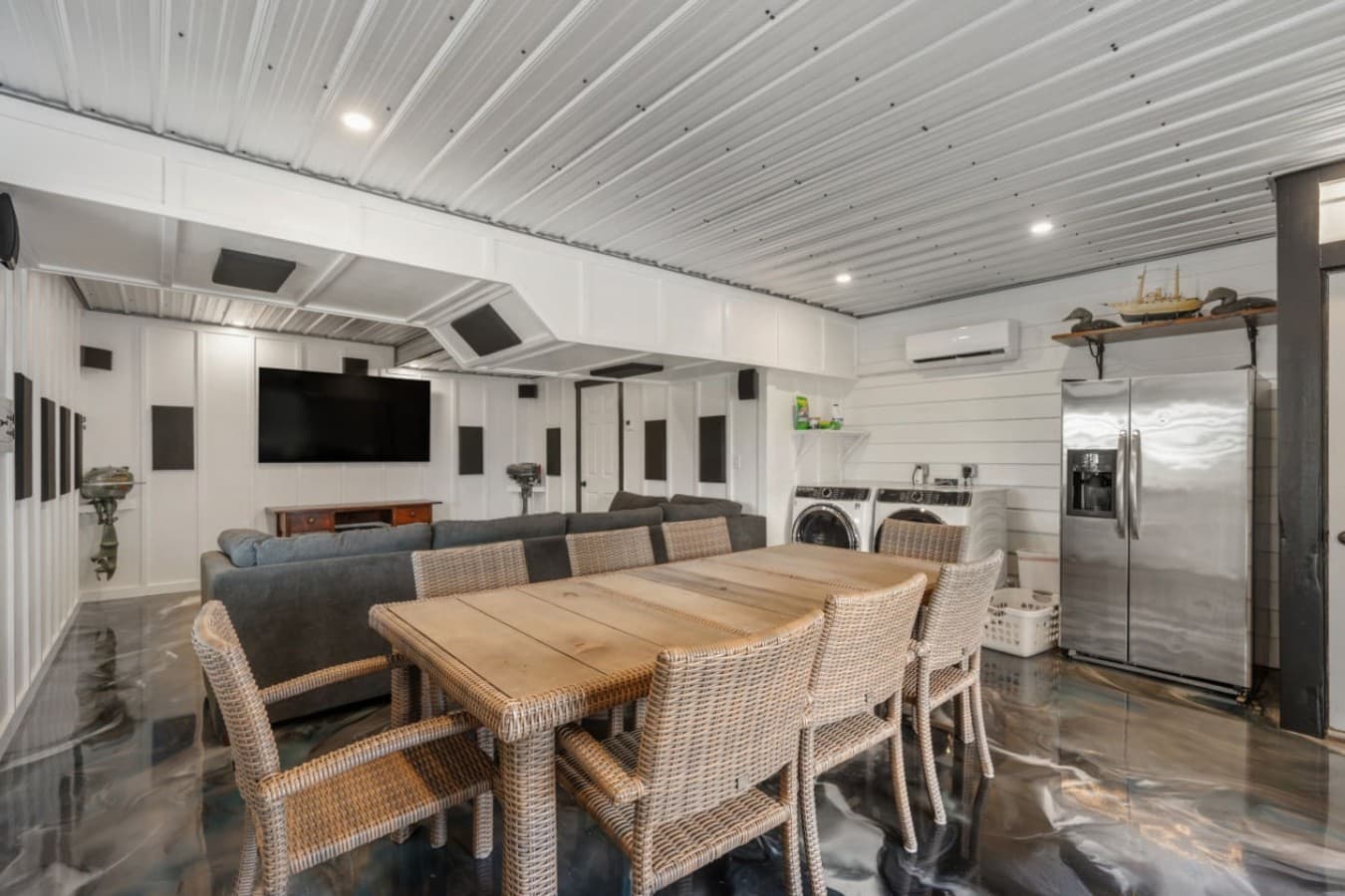 Garage rec room w/ a long dining table, sectional seating, wall TV & laundry alongside.
