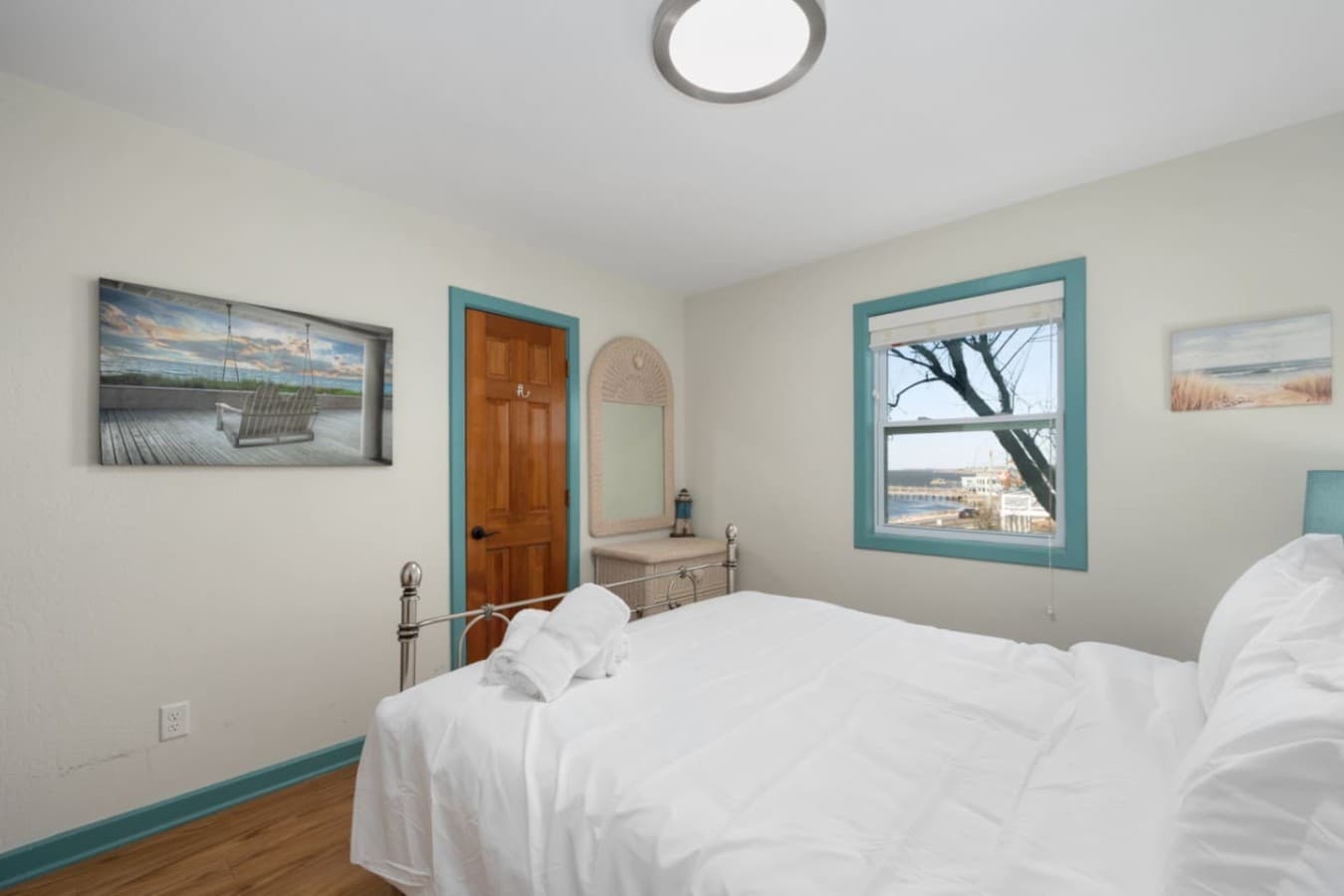 Cozy bedroom w/ white bedding, coastal wall art, & soft natural light for a calm retreat.