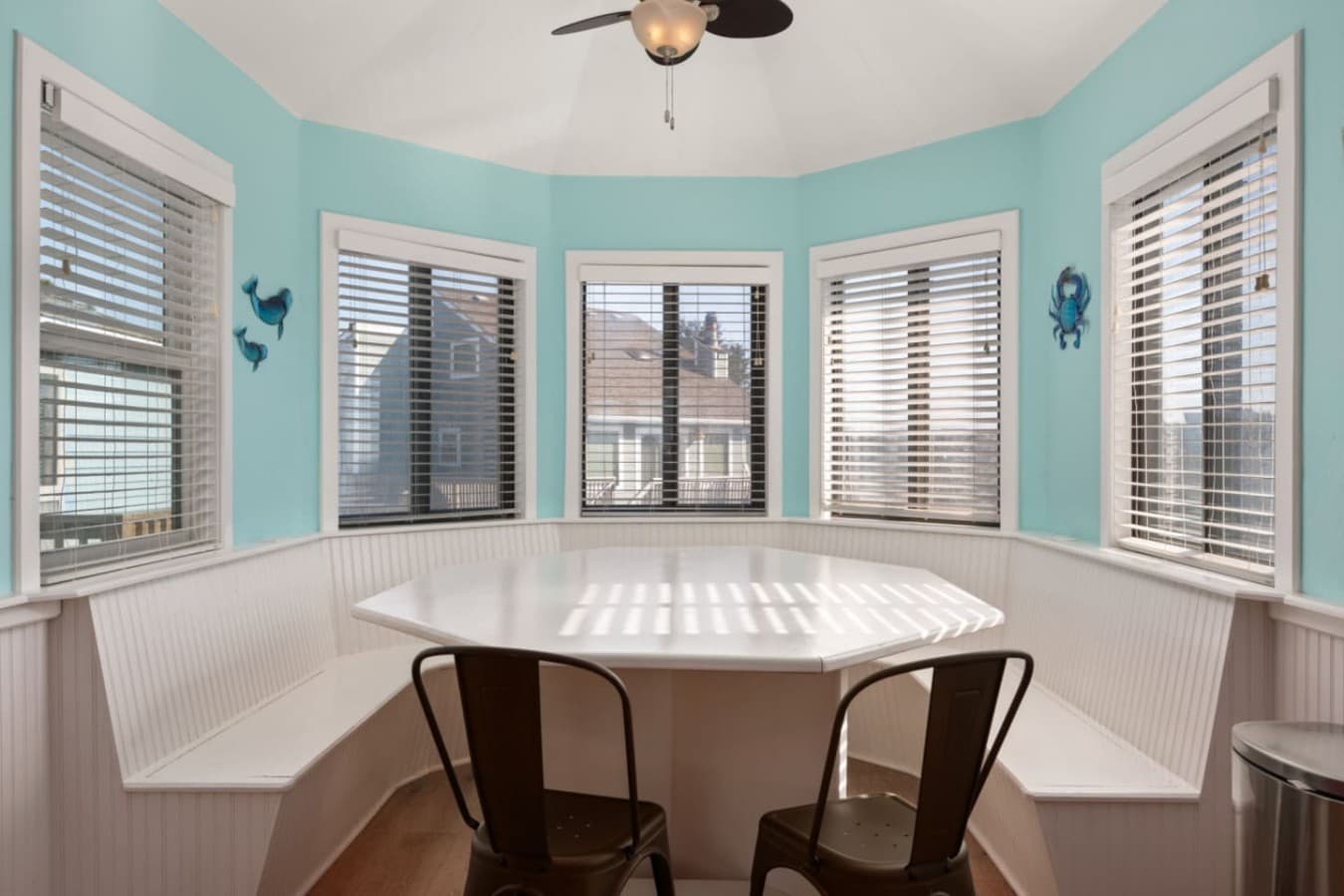 Sunlit dining nook w/ wraparound windows & coastal tones, a bright spot for coffee or casual meals.