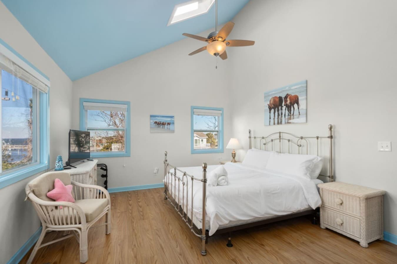 Bright bedroom w/ white bedding, beach art, & soft light for restful coastal nights.