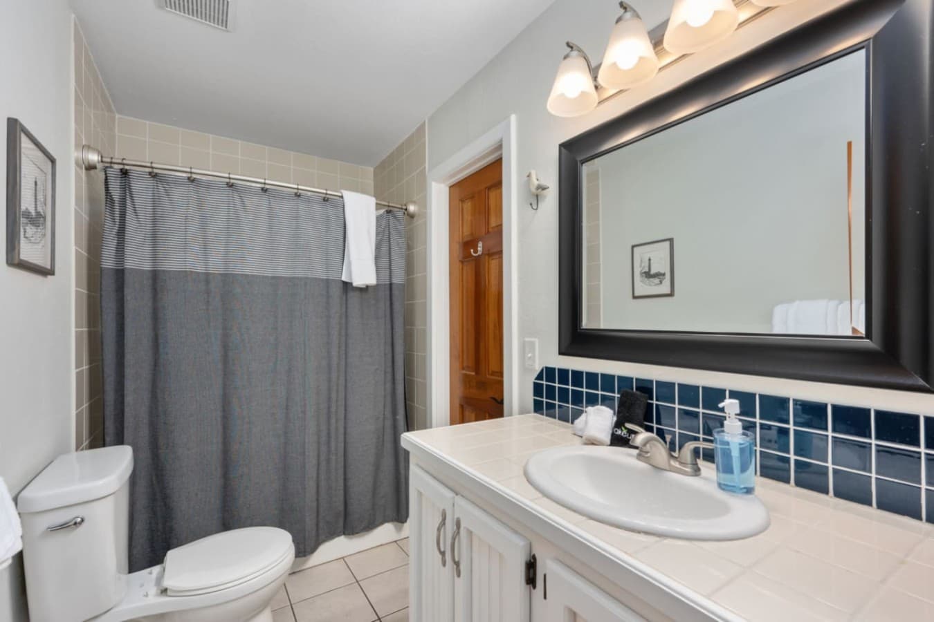 Bathroom w/ clean vanity, tub-shower combo, & simple coastal details.