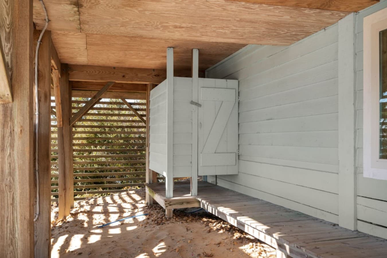 Covered outdoor nook w/ privacy panels, wood flooring, & filtered sunlight for a relaxed, beachy feel.