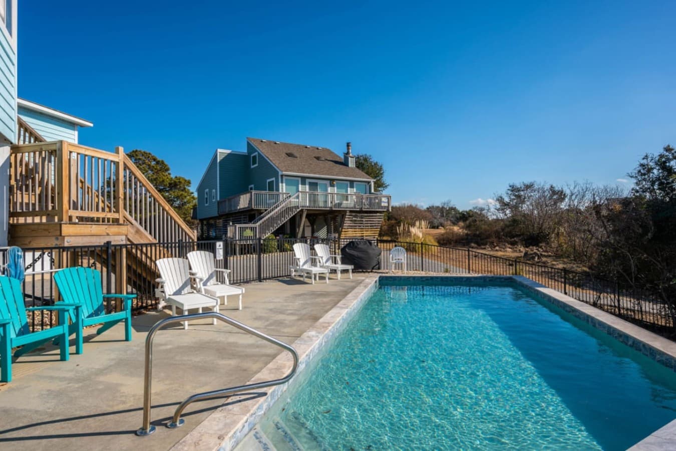 Pool w/ Adirondack chairs & loungers, backed by the home's stacked decks.