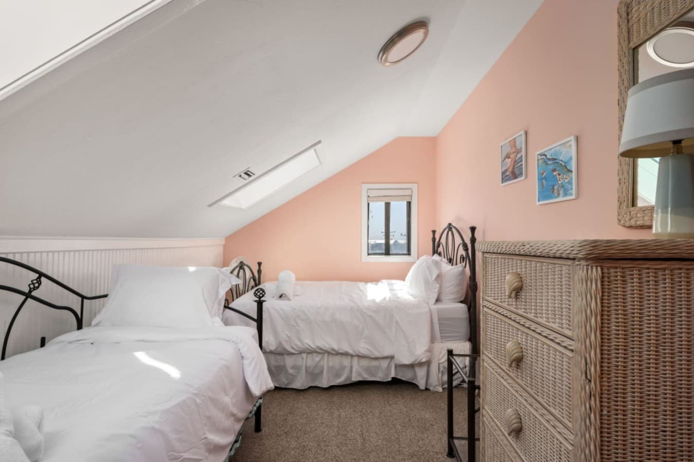 Top-floor bedroom under a sloped ceiling w/ two single beds, wicker dresser & a skylight.