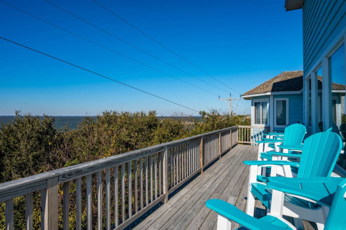 Sound-view deck w/ a row of turquoise Adirondack chairs along the rail.