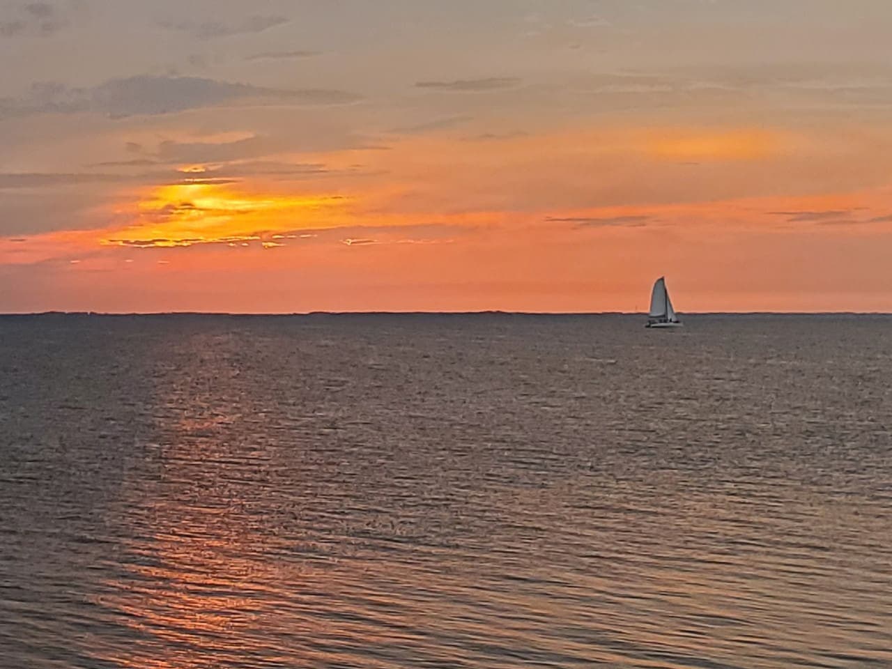 Sunset over the sound w/ a lone sailboat out on the flat water.