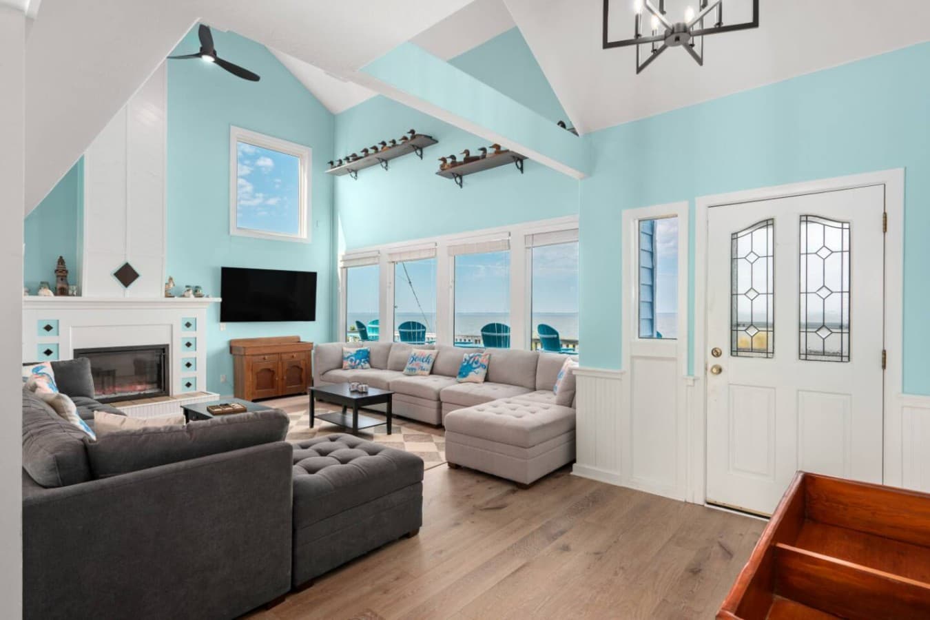 Living room w/ vaulted ceiling, sectional seating, fireplace & a wall of sound-facing windows.