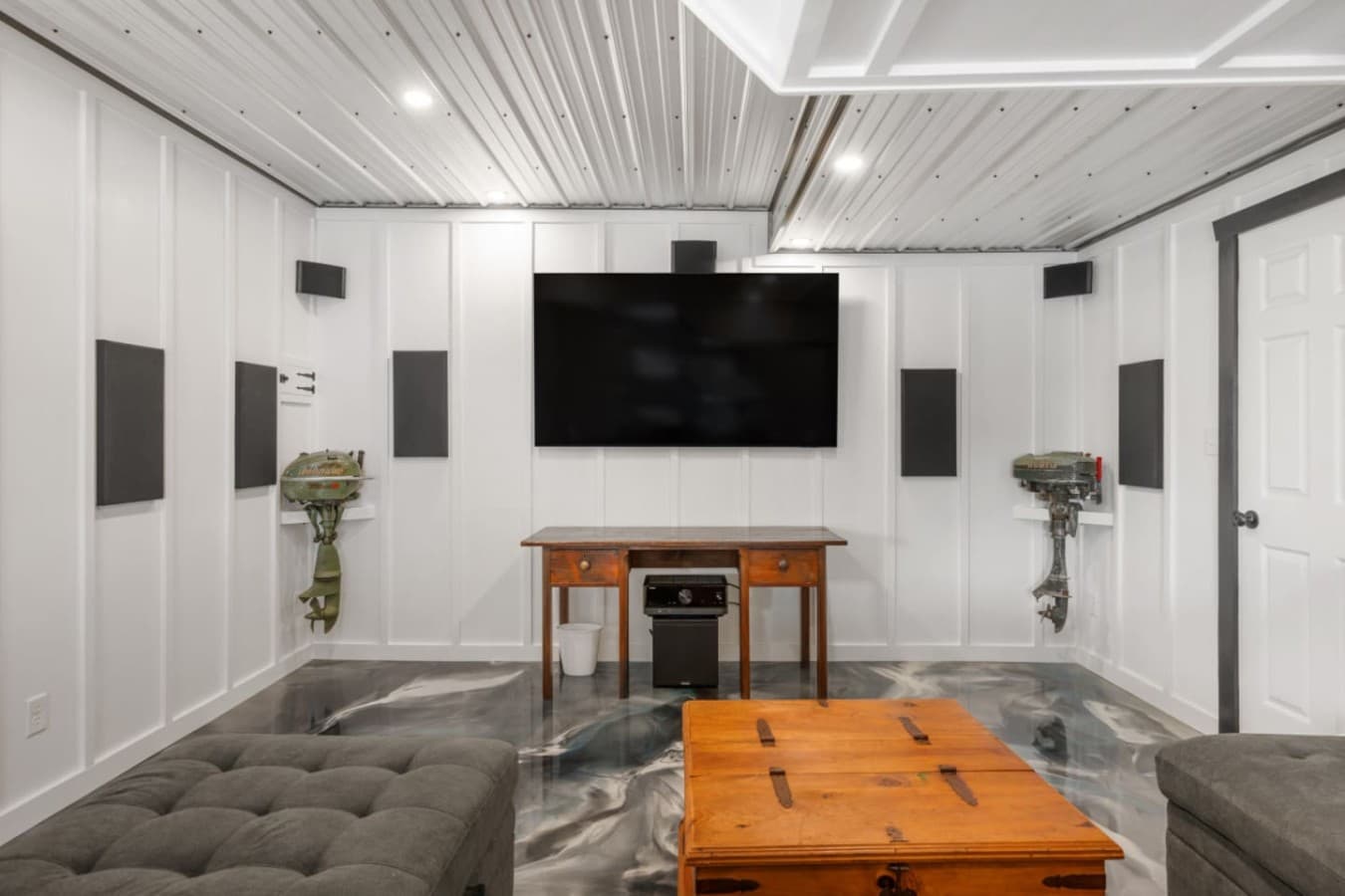 Garage rec room w/ a sectional, mounted TV, surround speakers & a wood trunk coffee table.
