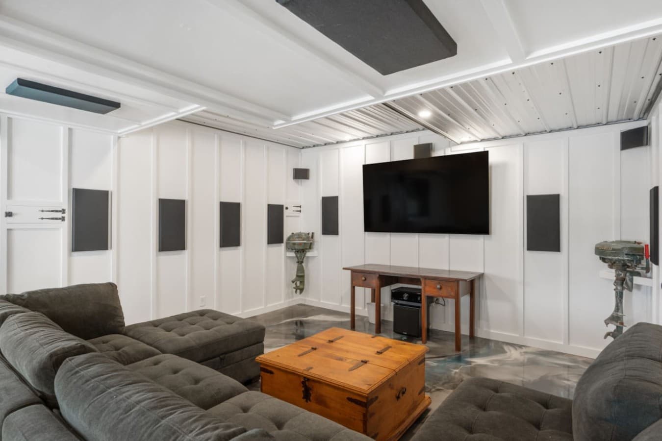 Garage rec room w/ deep sectional seating facing a mounted TV & surround speakers.