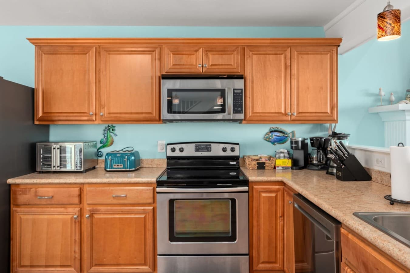 Kitchen w/ wood cabinetry, stainless range & microwave, toaster oven & coffee station.