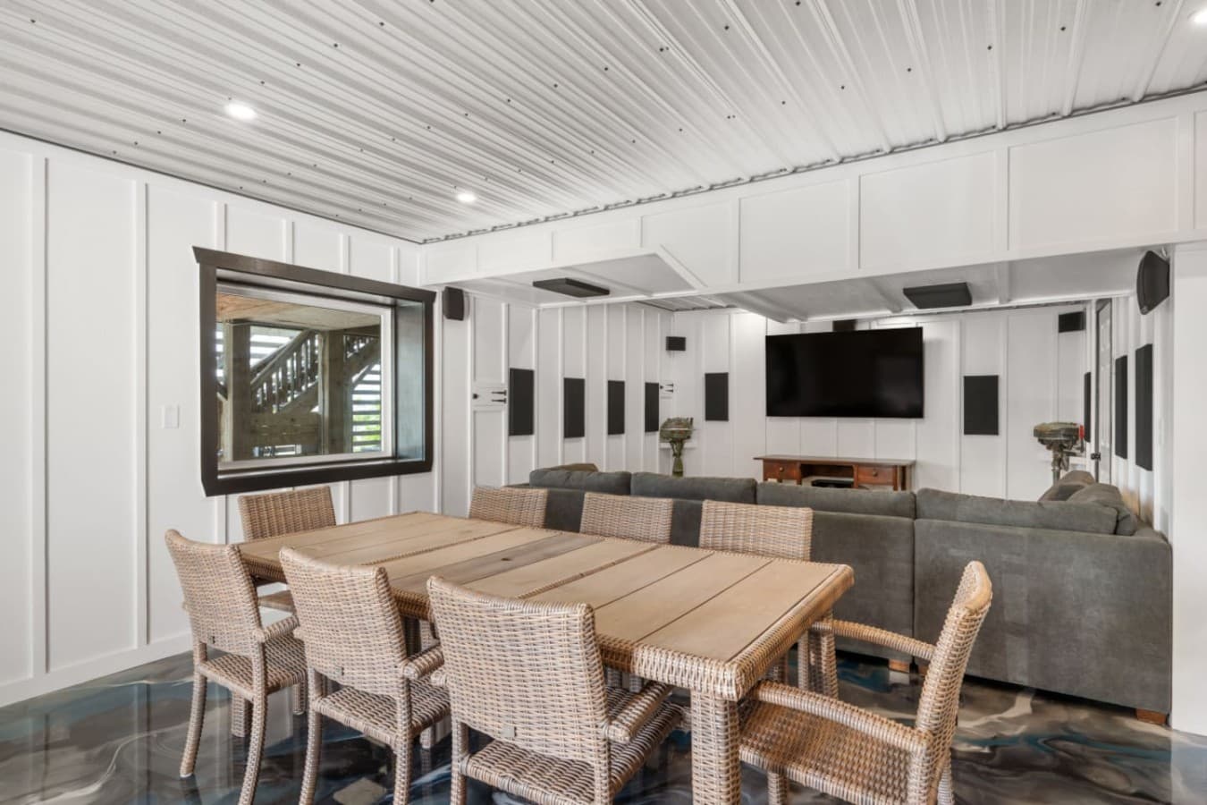Garage rec room set up w/ a long dining table, wicker chairs & a sectional under the TV.