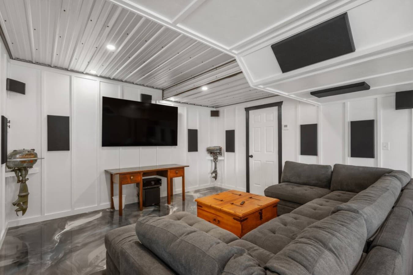 Garage rec room w/ an L-shaped sectional, mounted TV & mounted speakers on white shiplap.