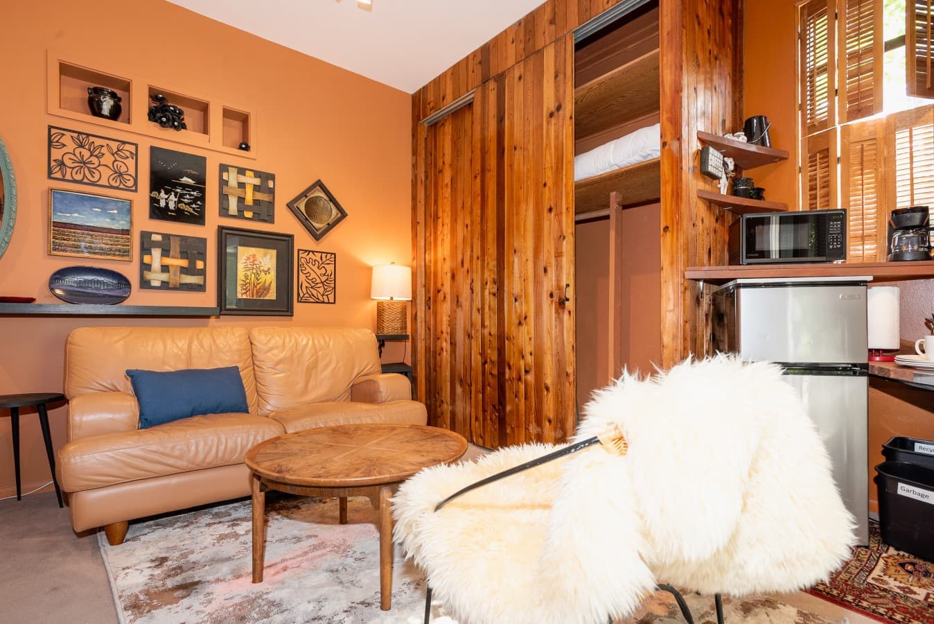 This cozy boho-style studio features a warm and inviting living area with a soft leather loveseat, a rustic wooden coffee table, and a stylish accent chair draped with faux fur,  perfect for relaxing or reading. .jpg