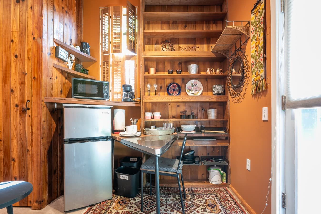 The kitchenette includes a mini fridge, microwave, coffee maker, dining table, and open shelves stocked with dishes and cookware, perfect for light meals..jpg
