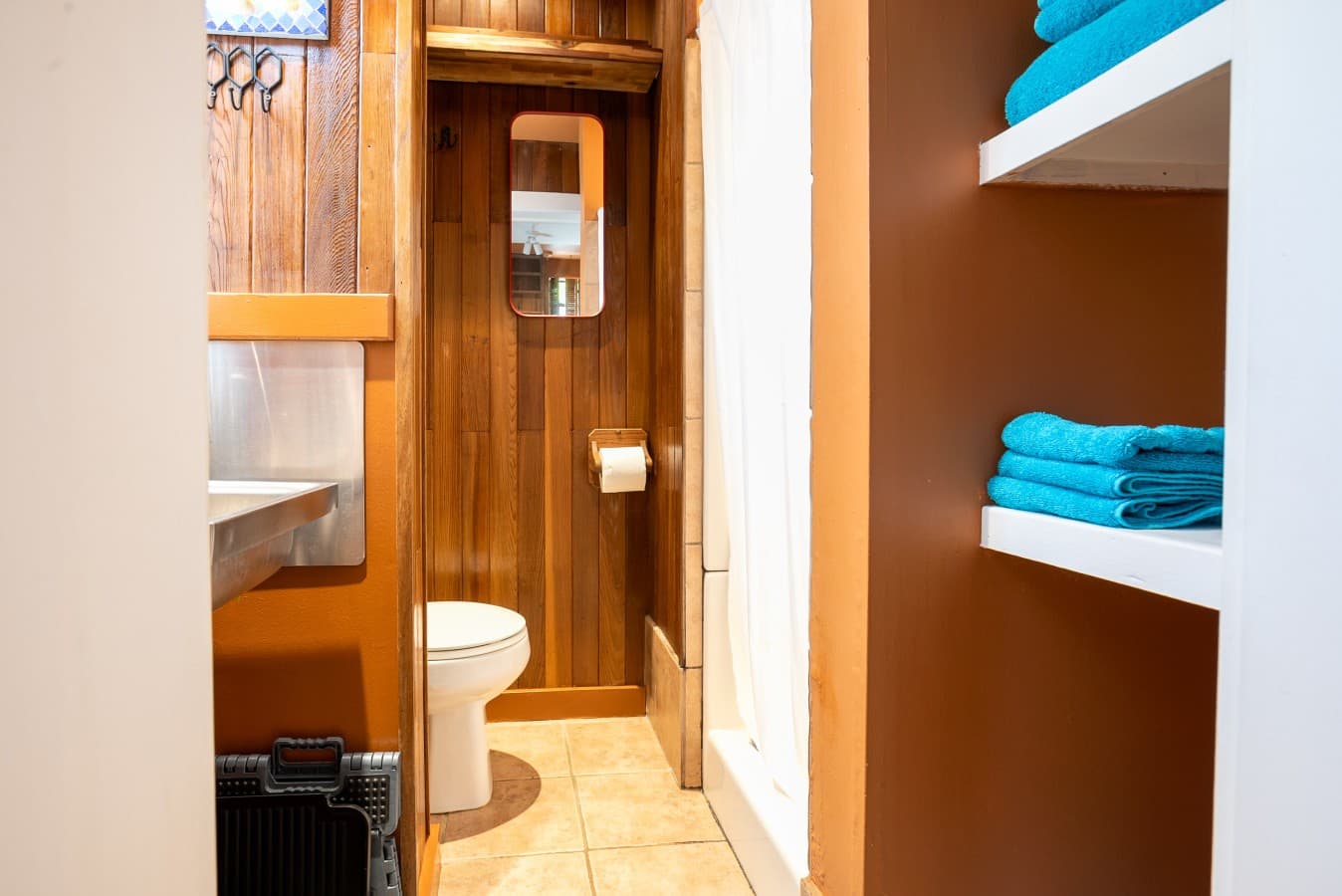 Compact bathroom with rustic wood paneling, a stainless steel sink, a toilet, and natural light. Simple, functional, and cozy,  designed with charm and practicality in mind..jpg