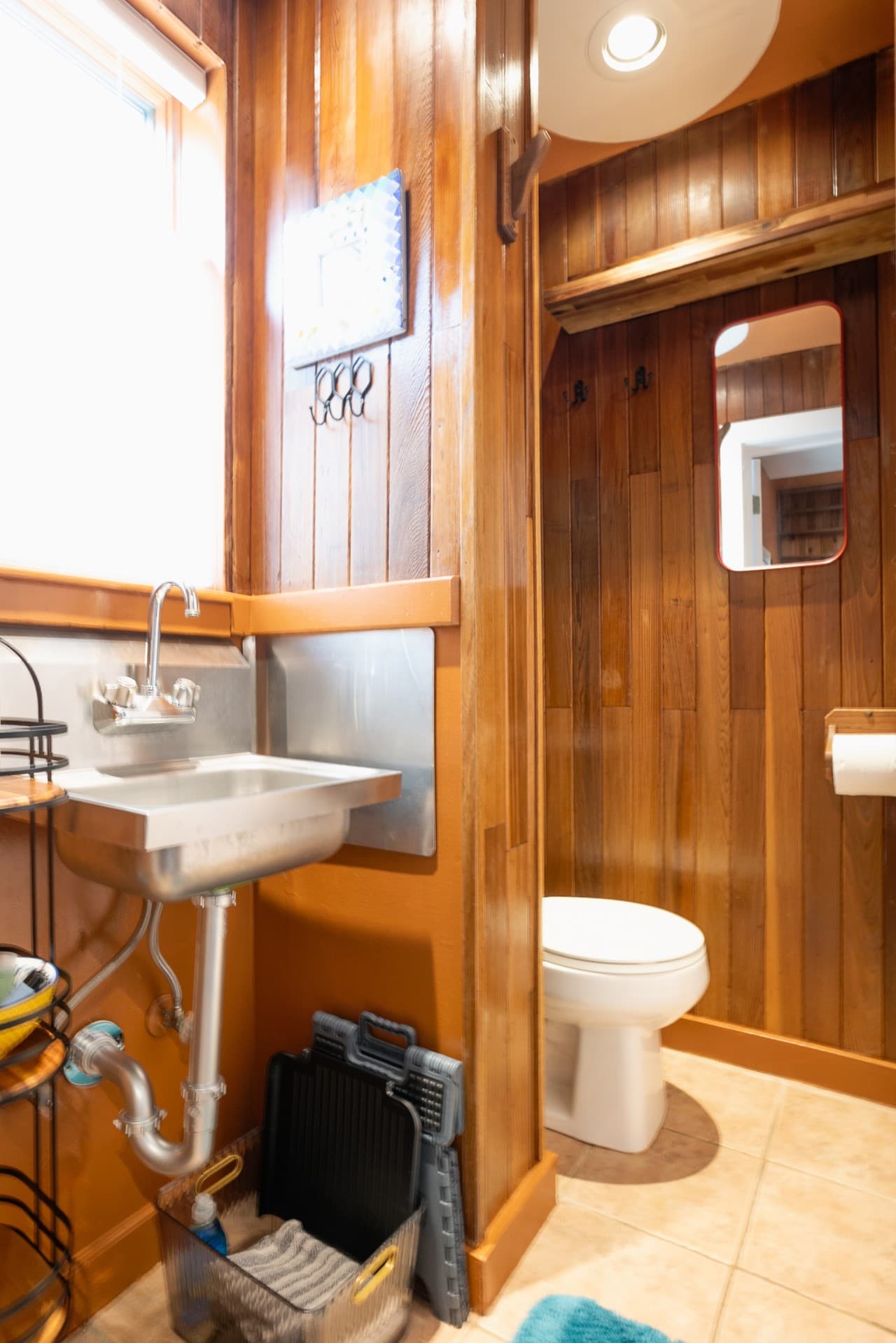 Compact bathroom with rustic wood paneling, a stainless steel sink, toilet, and natural light. Simple, functional, and cozy — designed with charm and practicality in mind..jpg