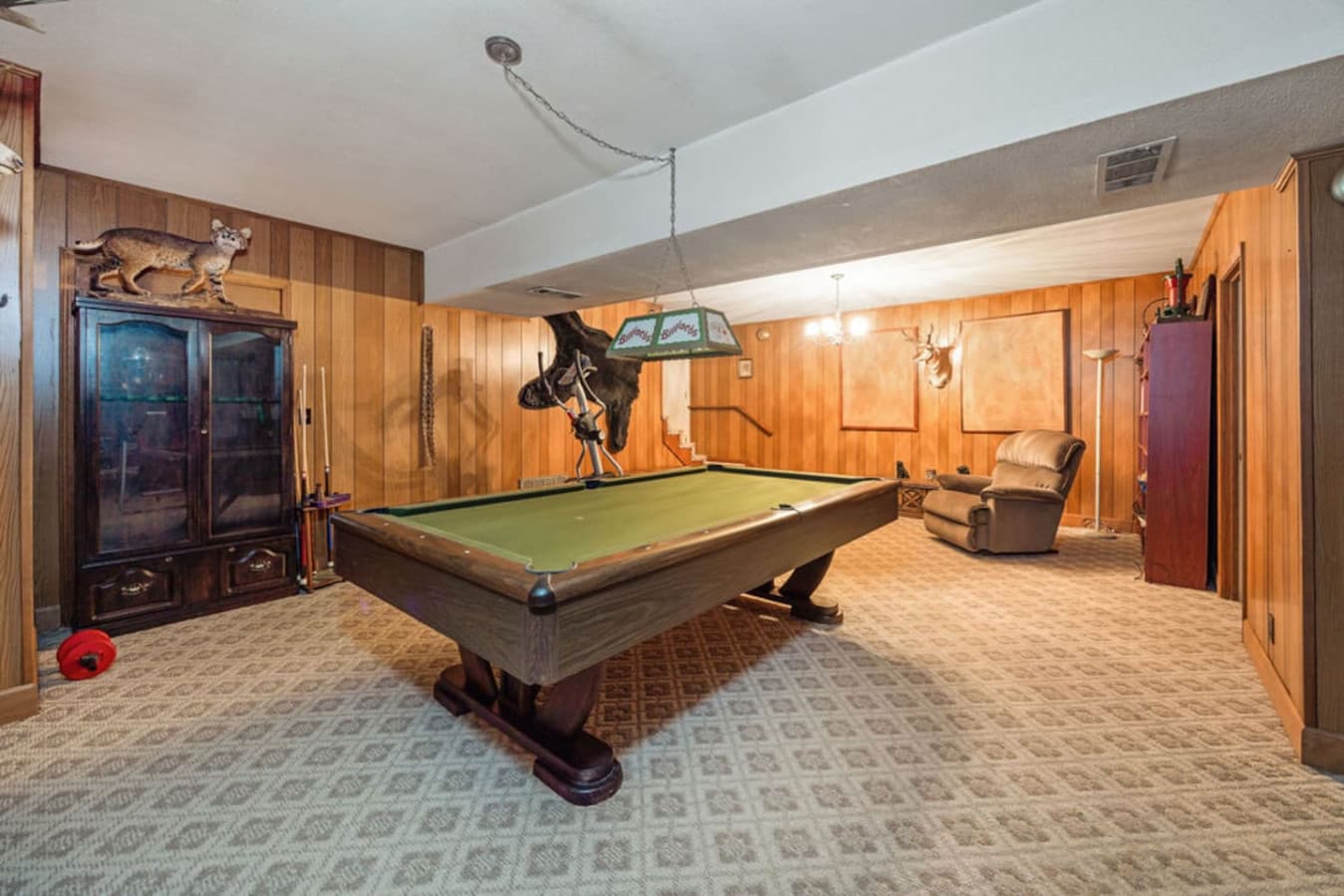 A game room with a full size pool table and comfortable seating.