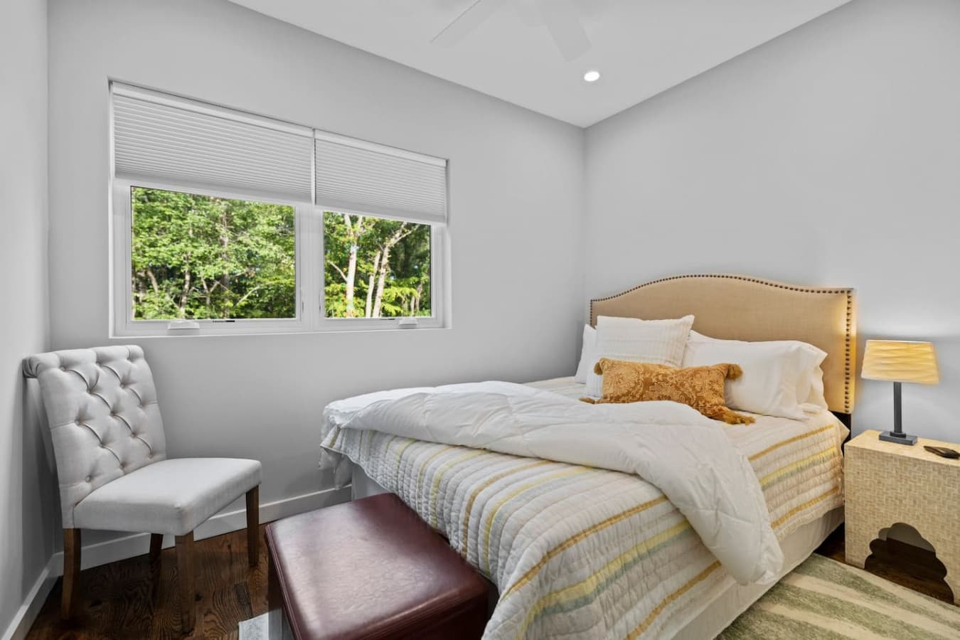 Comfortable second bedroom with a queen bed, Smart TV, ceiling fan, closet, nightstands, charging dock, white noise machine, and a cozy storage ottoman.
