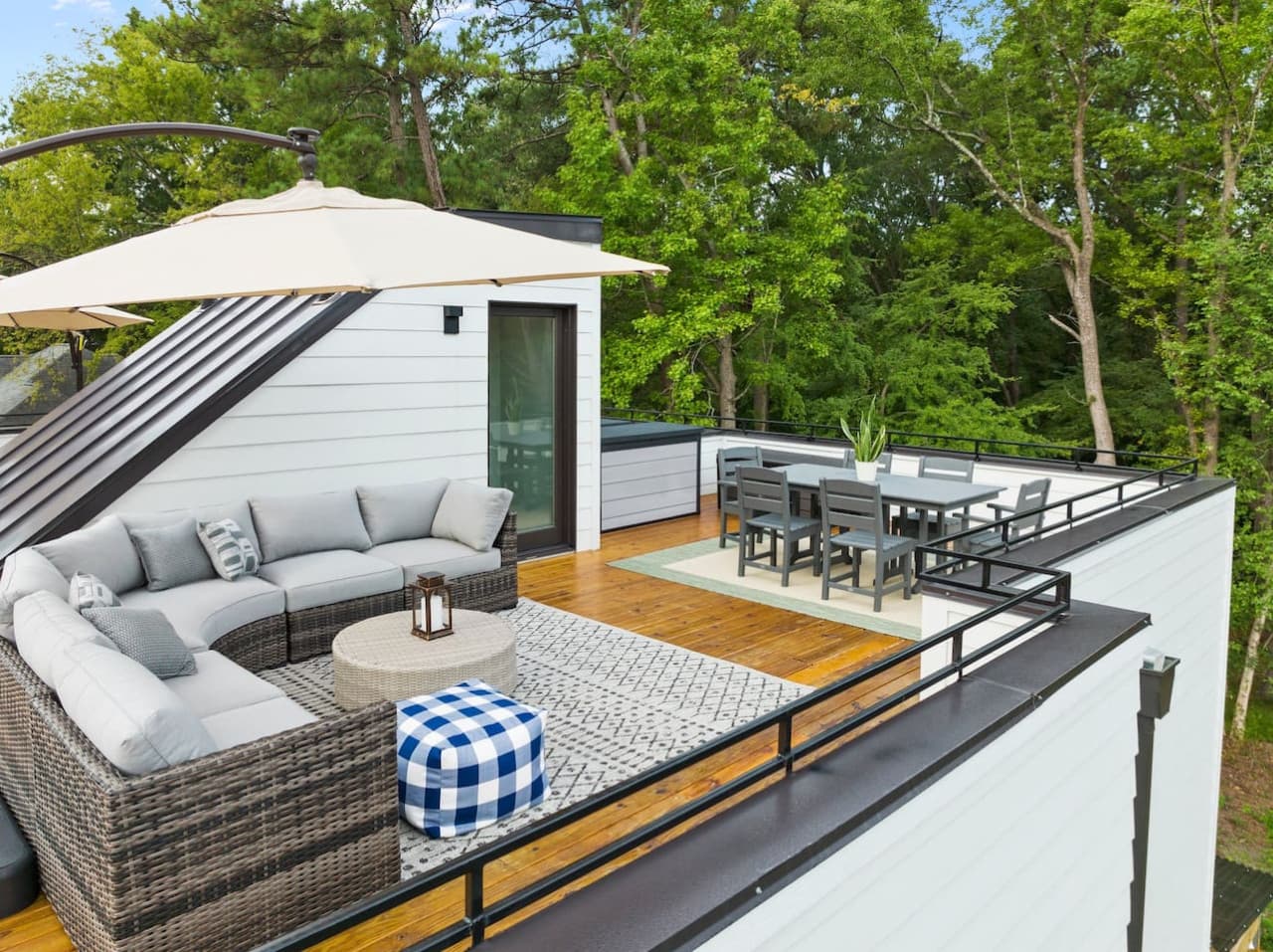 Escape to this private rooftop retreat nestled among the trees, featuring a cozy sectional sofa, umbrella-shaded lounge area, and stylish dining setup for six.