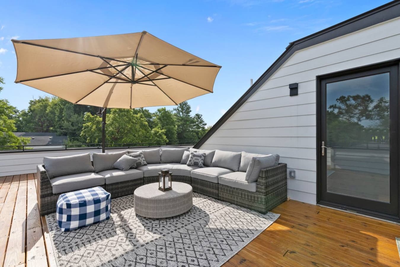 Unwind on this stylish rooftop lounge featuring a spacious wicker sectional with plush cushions, a large umbrella for shade, a cozy outdoor rug, and a chic coffee table centerpiece.