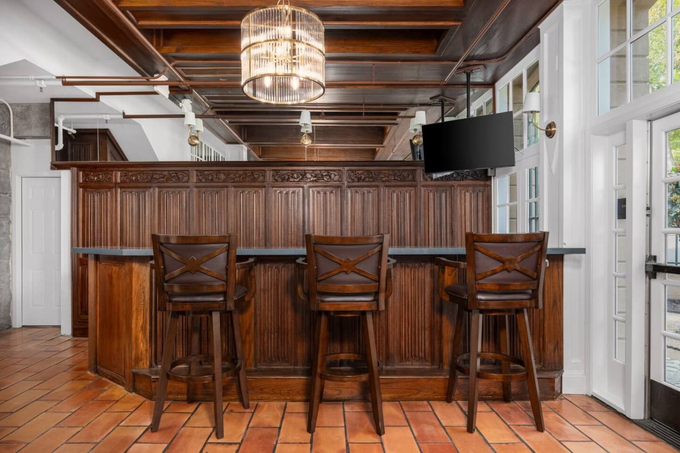 A classic shared bar seating area with rich wood details and a mounted television located in the hotel’s common area and not inside your private room.