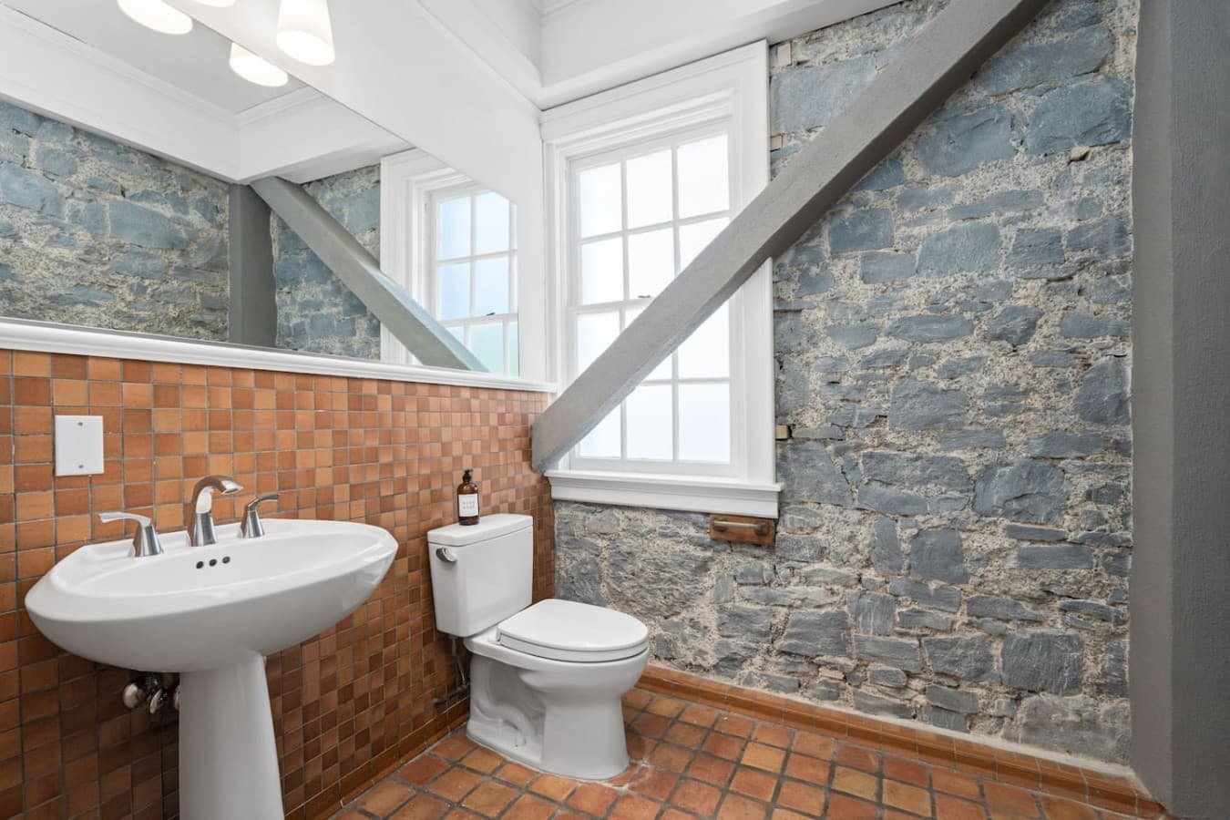 This is the private bathroom inside the room you will be renting featuring historic stone details, warm tile flooring, and a clean pedestal sink.