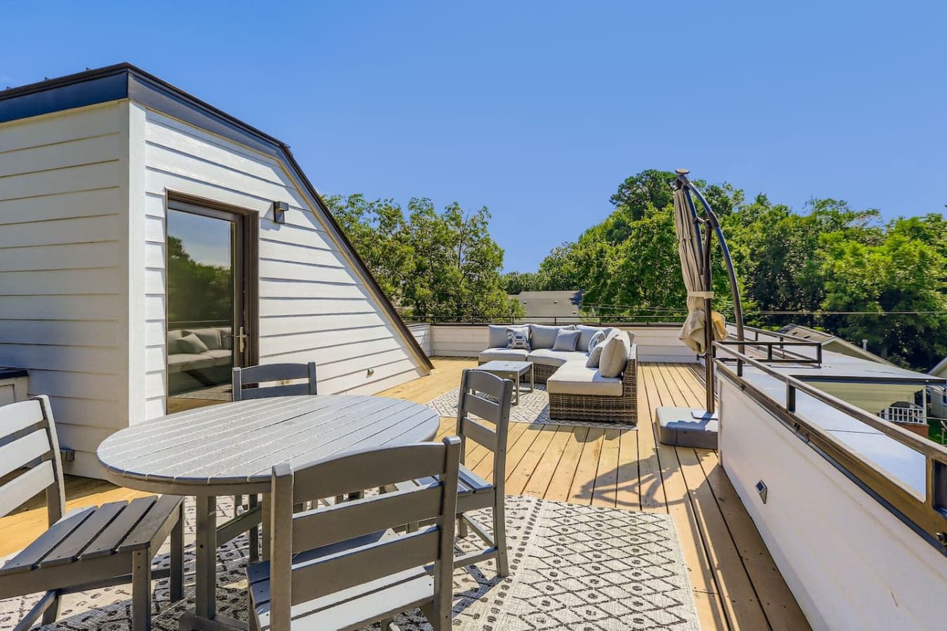 Escape to this private rooftop retreat nestled among the trees, featuring a cozy sectional sofa, umbrella-shaded lounge area, and stylish dining setup for six.